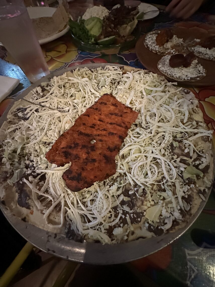 A tlayuda served open-faced like a pizza, this one is topped with black beans, quesillo cheese, cabbage and Cecina, or Oaxacan-style thin sliced pork.