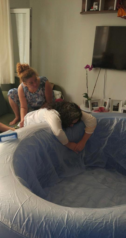 Photograph of two women indoors, one leaning over an inflatable pool.