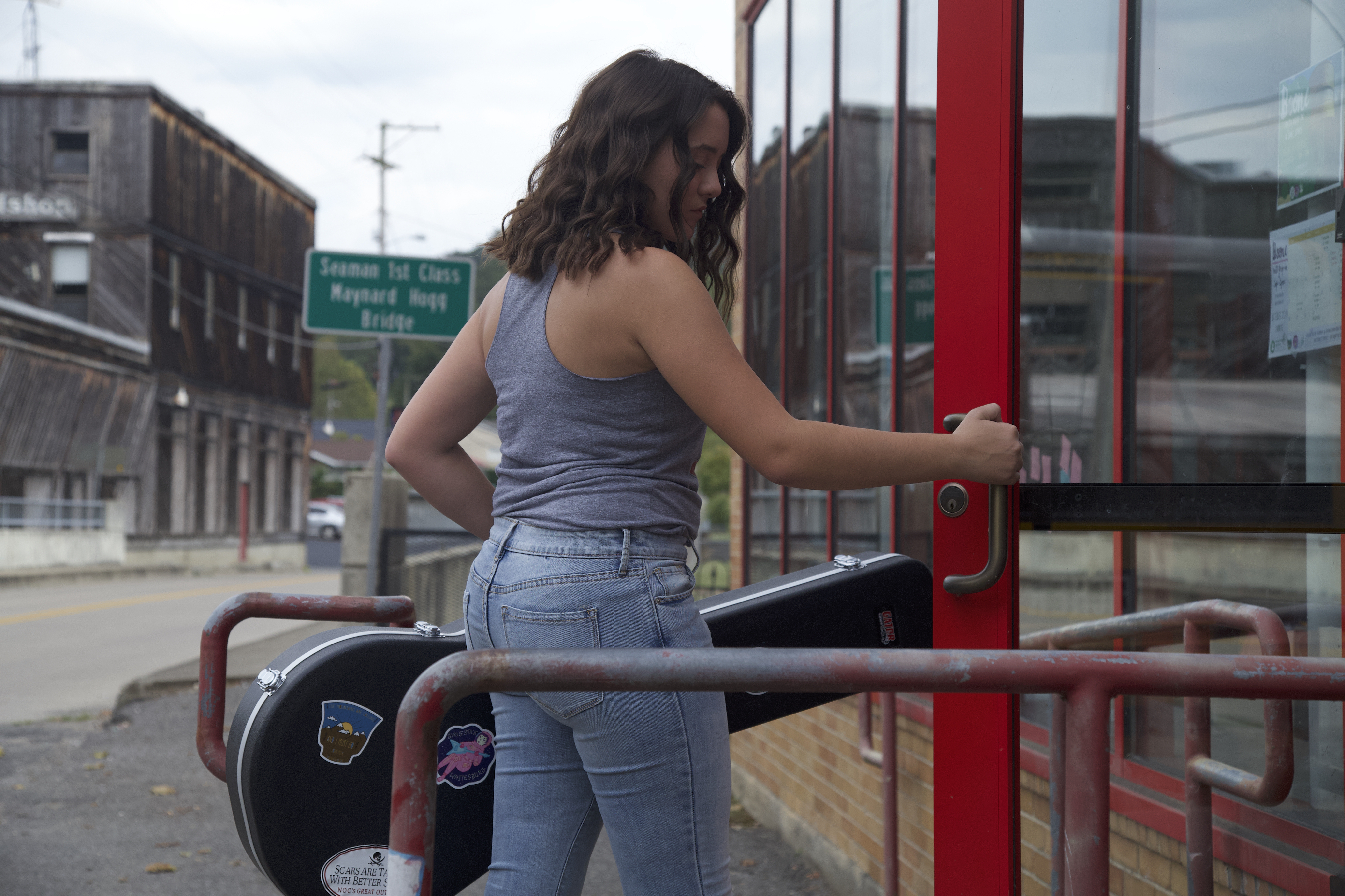 Photo of a woman carrying a guitar case entering a building