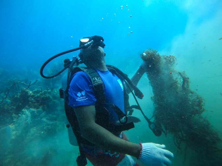 Photograph of a diver pulling up a ghost net from the seafloor
