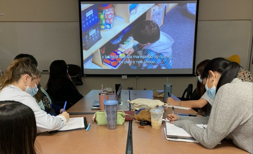 Photograph of people sitting at a table watching a screen