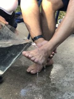 Photo of one hand lifting someone's foot and pouring water from a pitcher over it.