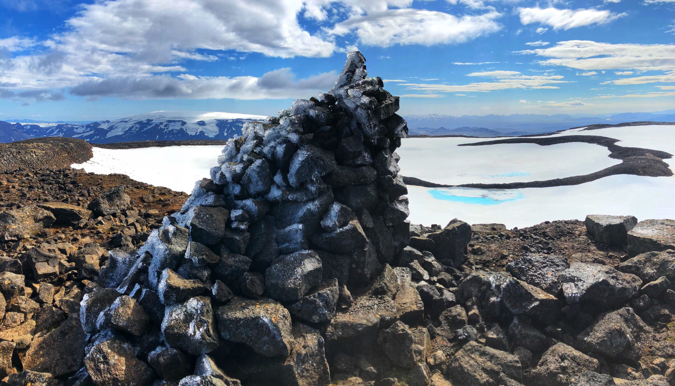 Photograph of a glacier with rocks in the foreground and a cloudy sky at the horizon.